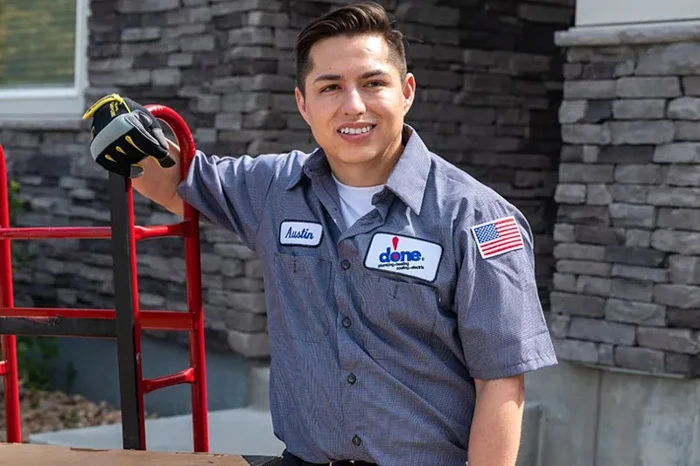 A smiling Done technician named Austin rests his arm on a hand truck loaded with an equipment box outside a home in Aurora, Colorado.