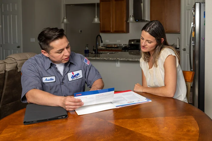 Done technician shows service documents to a homeowner seated at a kitchen table in an Aurora home.