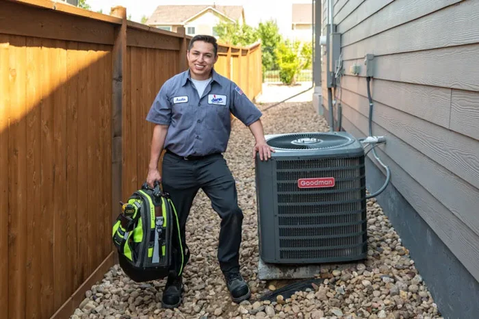 A Done technician with a tool backpack rests a hand on a Goodman outdoor AC unit beside a home in Aurora, Colorado.