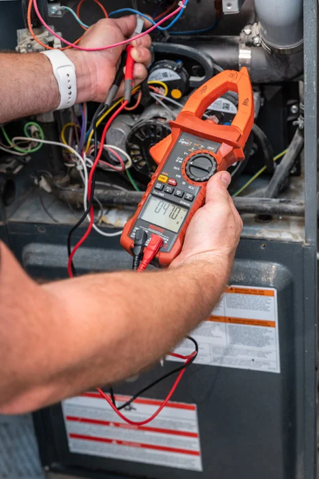 A Done technician holds an orange clamp meter and red test leads to diagnose an open furnace in an Aurora home.