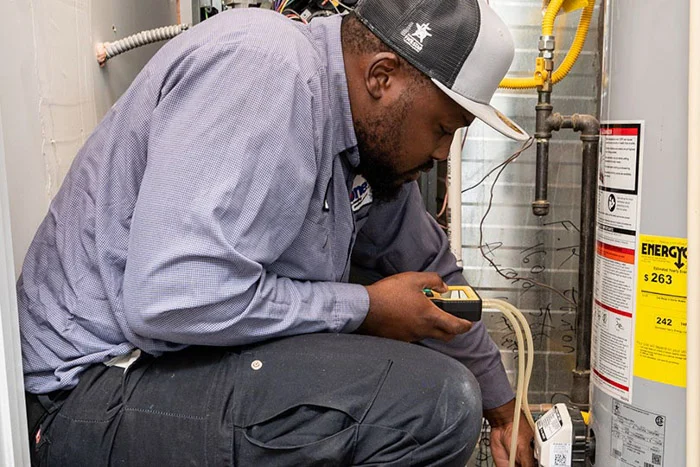 Done technician holding a diagnostic meter while checking wiring on a gas water heater in a Denver utility closet.