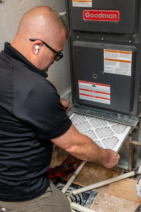 Done HVAC technician removing the pleated air filter from a Goodman furnace during maintenance at an Aurora home.
