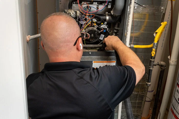 Done HVAC technician servicing the blower motor and colorful wiring inside an open furnace at an Aurora home.