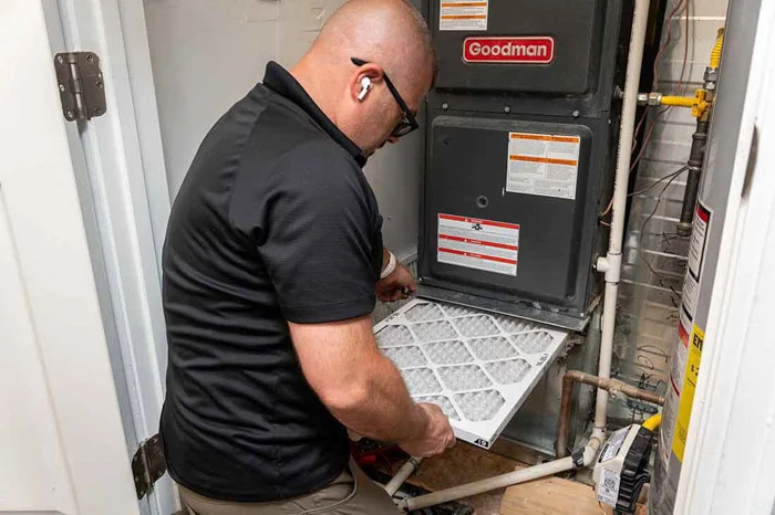 Done HVAC technician changing the air filter on a Goodman furnace in an Aurora home utility closet with copper piping.
