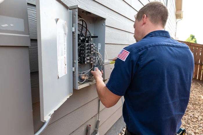 A Done electrician with a flag patch works on the wiring inside an open exterior electrical panel at an Aurora home.