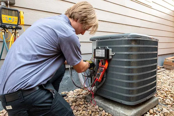 Done technician using a multimeter and gauges to service an outdoor air conditioning condenser beside the house in Denver, Colorado.