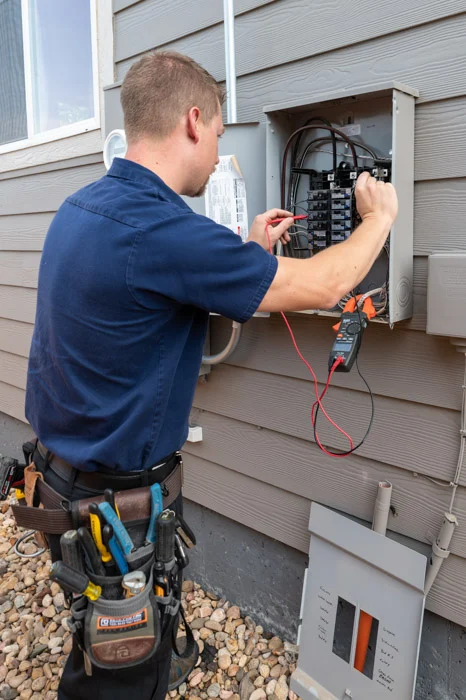 A Done electrician works on circuit breakers in an open exterior panel with a clamp meter on an Aurora home.