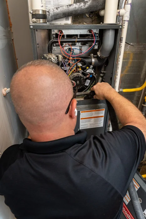Done HVAC technician reaching into the open burner and motor compartment of a furnace during service at an Aurora home.