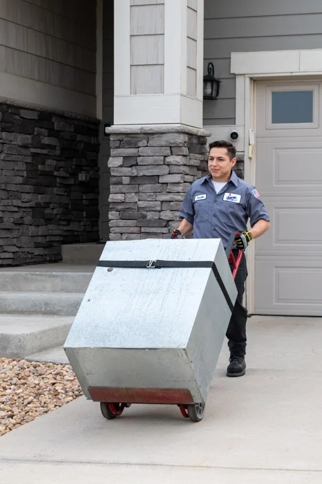 A Done technician wheels a metal furnace unit on a hand truck toward the front entrance of an Aurora, Colorado home.