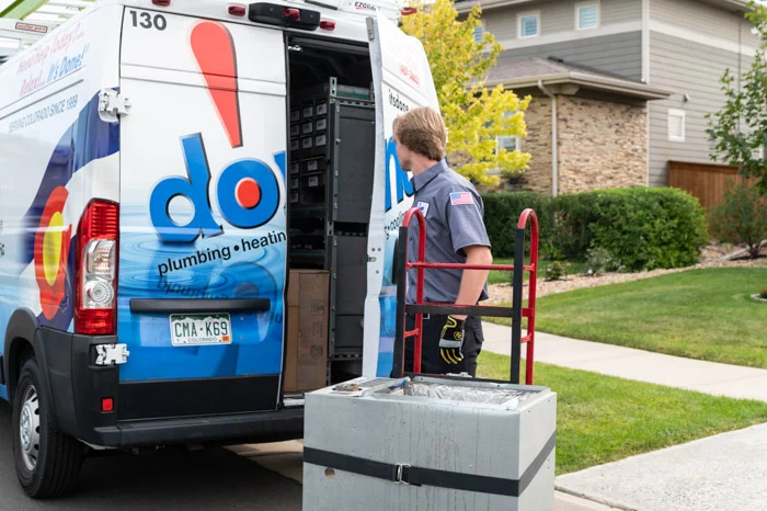 A Done technician stands at the open rear of a parts-stocked service van with a furnace unit nearby in Denver, Colorado.