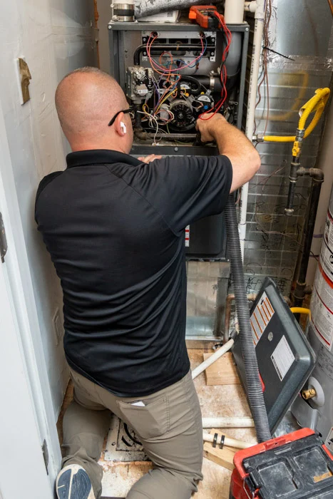 Done HVAC technician working on the open wiring of a furnace inside an Aurora home utility closet next to a water heater.