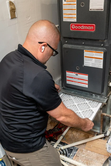 Done HVAC technician sliding a new pleated air filter into a Goodman furnace during a tune-up in a Denver home.