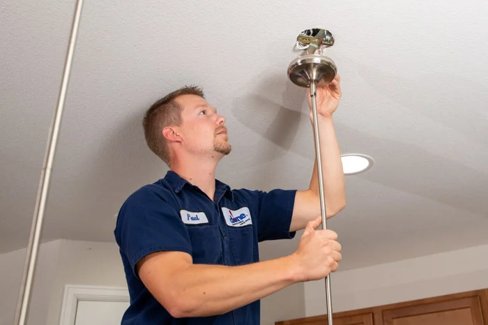 Done technician Paul lifts a pendant light fixture toward a ceiling junction box during installation in an Aurora home.