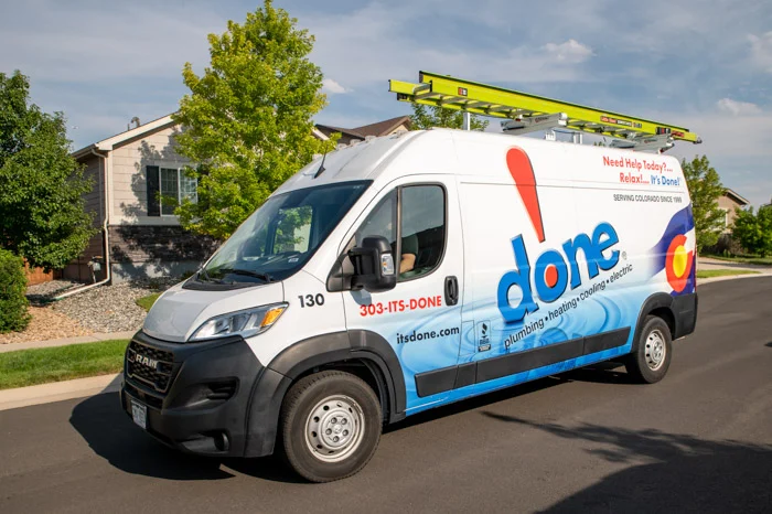 A white Done service van with roof ladder rack parked along a residential street in Aurora, Colorado.