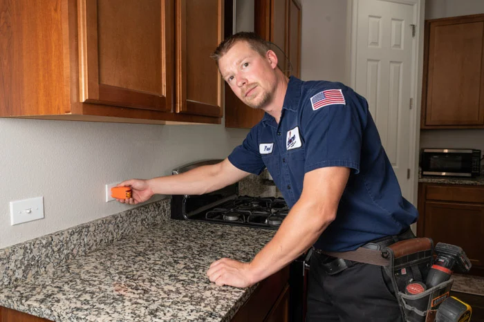Done electrician using an orange voltage tester on a kitchen outlet near the stove in an Aurora home.