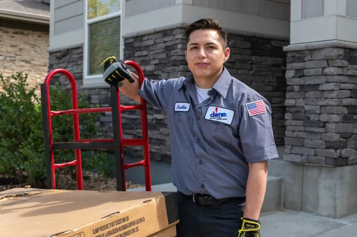 A Done technician named Austin rests his gloved hand on an empty red hand truck beside an equipment box outside a Denver, Colorado home.