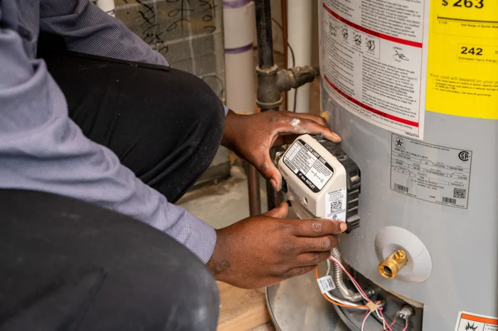Done technician handling the gas control valve on a gray water heater with the EnergyGuide label visible in Aurora.