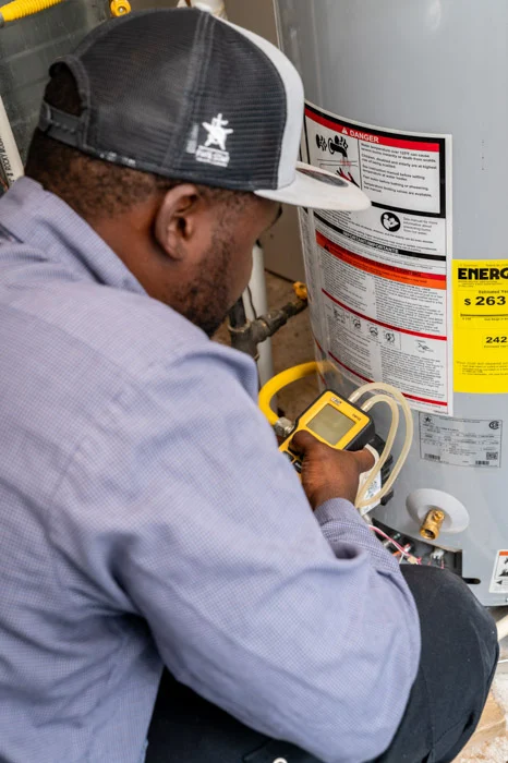 Done technician taking a meter reading on a gas water heater marked with a danger label in a Denver utility space.