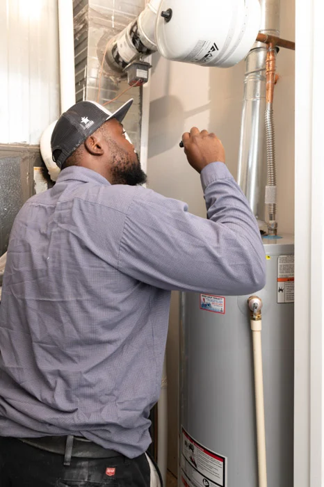 Done technician reaching up to inspect the flue venting and piping above a water heater in a Denver utility closet.