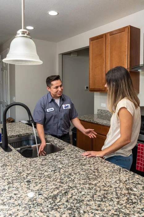 Done plumber standing at the kitchen sink talking with a homeowner across the granite island in a Denver home.