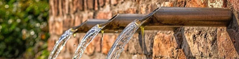 Clear water and oil dripping from pipes in a wall