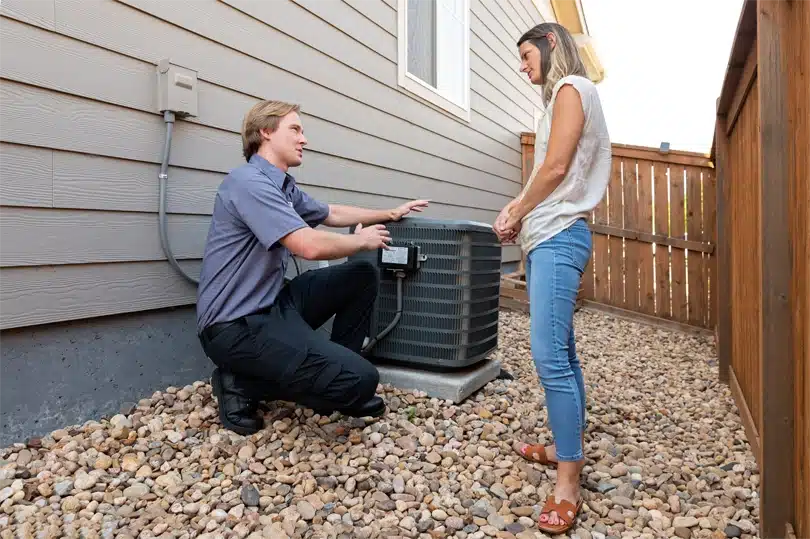 A Done HVAC technician kneels by an AC condenser to explain upgrades to a customer