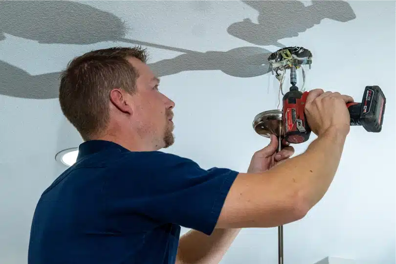A Done electrician uses tools to hang a ceiling fixture
