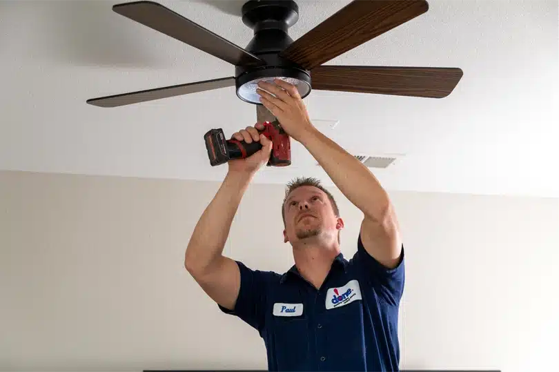 A Done electrician uses tools to screw a new ceiling fan into place