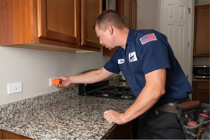 A Done electrician using tools to test power at an outlet in a kitchen