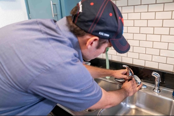 A Done plumber fixing a kitchen faucet