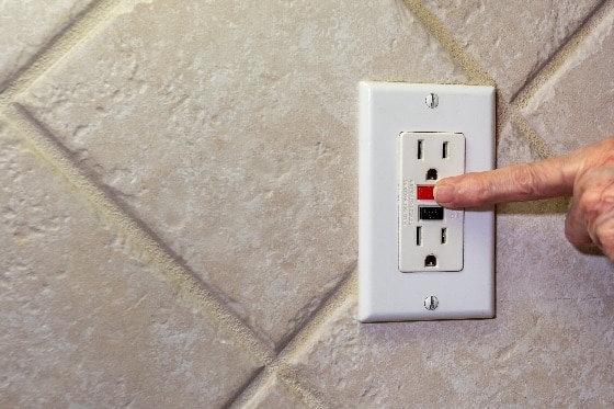 Someone testing a GFCI outlet on a wall