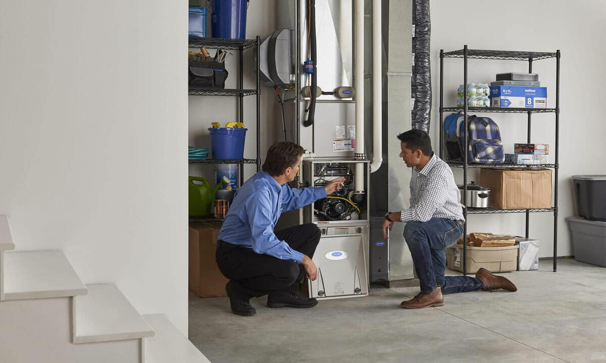 An HVAC technician and homeowner inspect a gas furnace