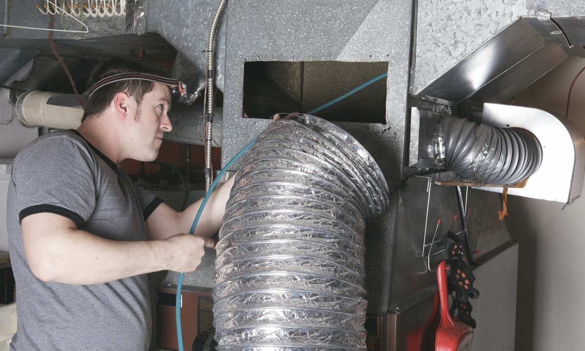 An HVAC technician repairing a furnace in an attic