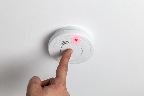 A stock photo of a finger testing a smoke detector