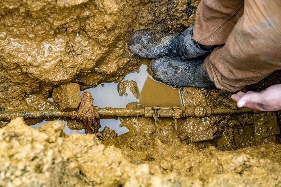 A photo of a technician standing in a mud next to a water line in a home