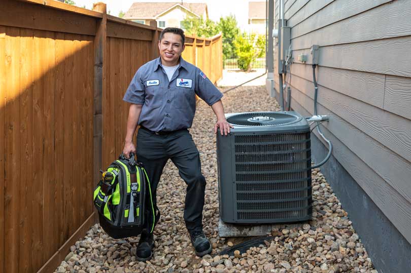A Done HVAC technician standing next to an AC outside a Denver home