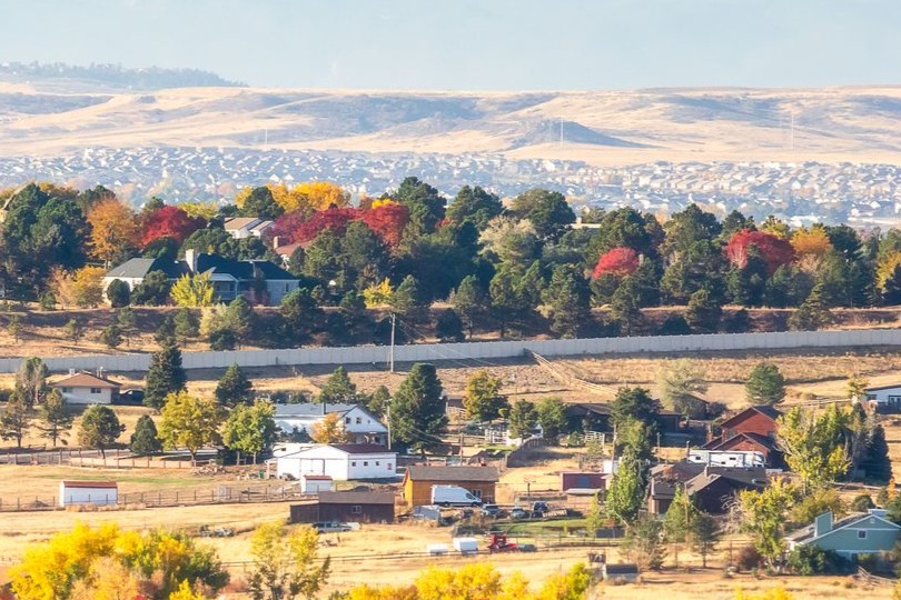 A fall scene of rural homes with color changing trees and mountains in the background
