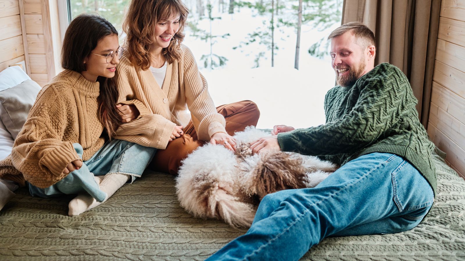 A family and their dog playing together on the ground in front of the snowy mountain scene in the window