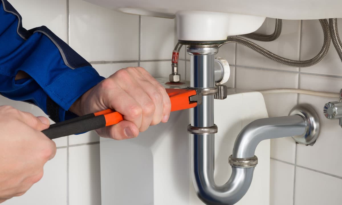 A plumber using a wrench on a pipe under a bathroom sink