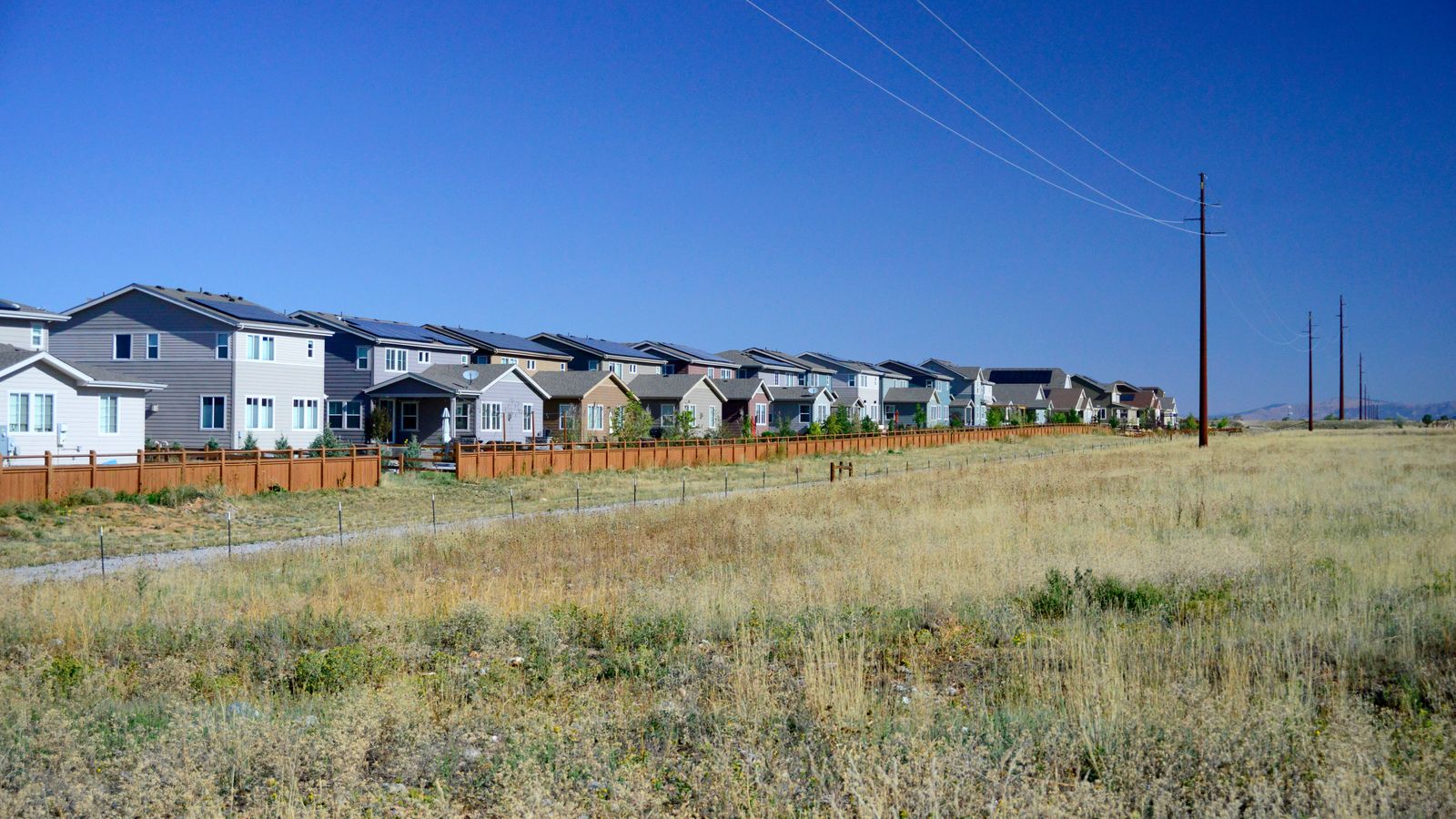 A row of homes across from an empty field with mountains in the background.