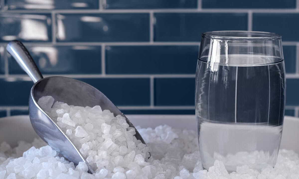 A scoop of salt and a glass of clean water to symbolize the purpose of water softener