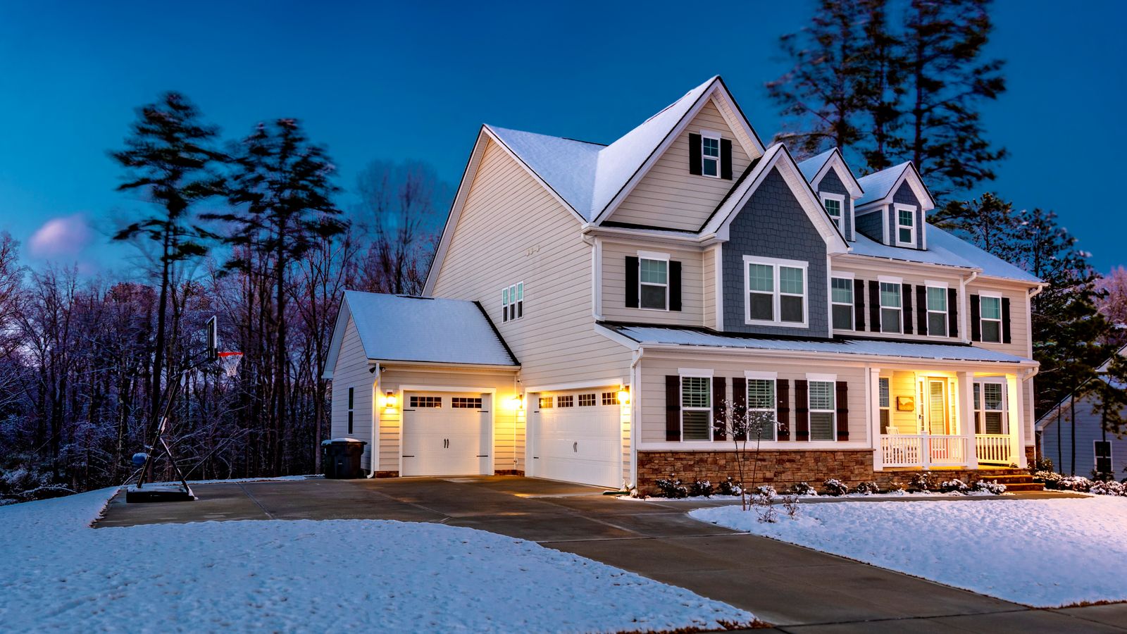 A night time photo of a home with its lights on and snow on the ground